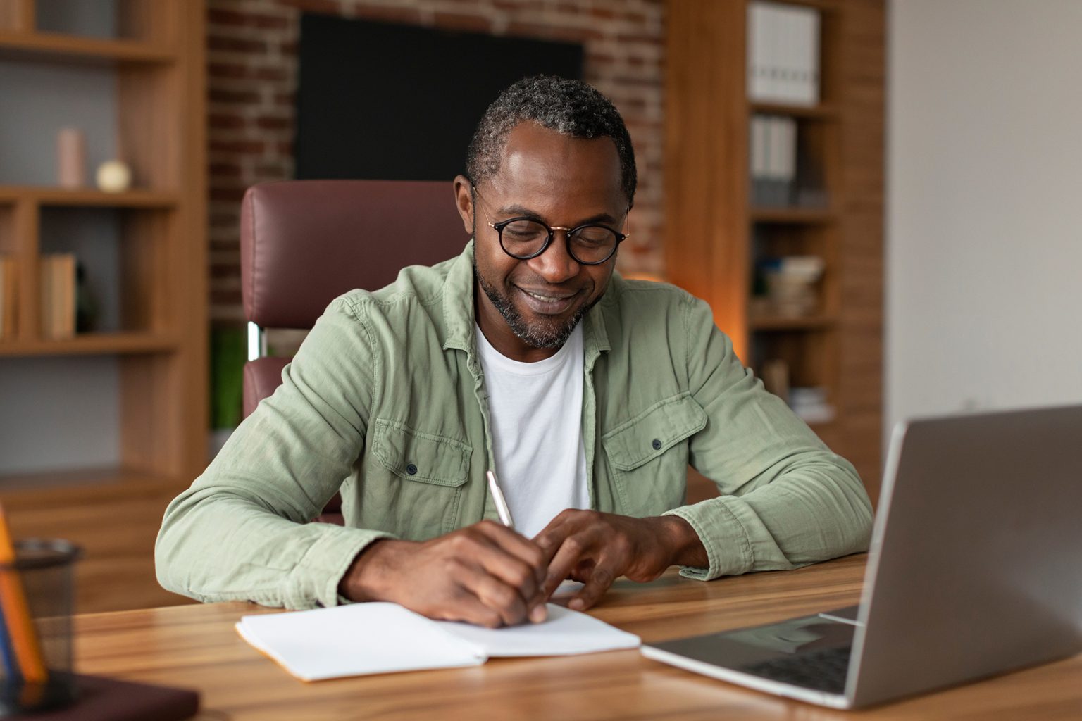 businessman in glasses making notes at table with laptop