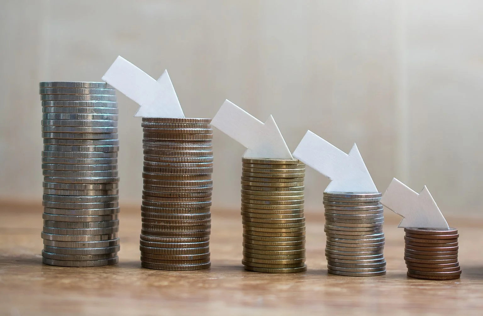 Piles of coins decreasing in size with arrows pointing down on top of each stack