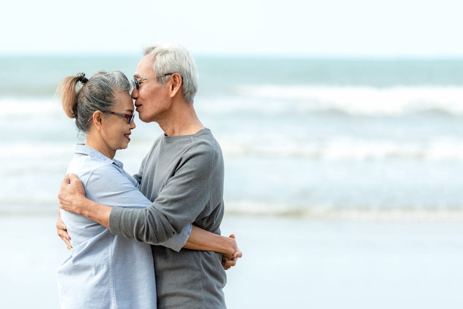 Senior couple hugging on a beach with waves in the background