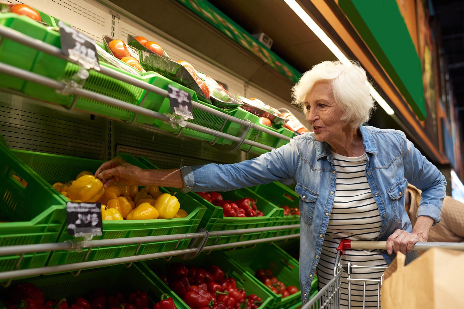 Portrait of modern senior woman with shopping cart choosing fruits and vegetables in supermarket