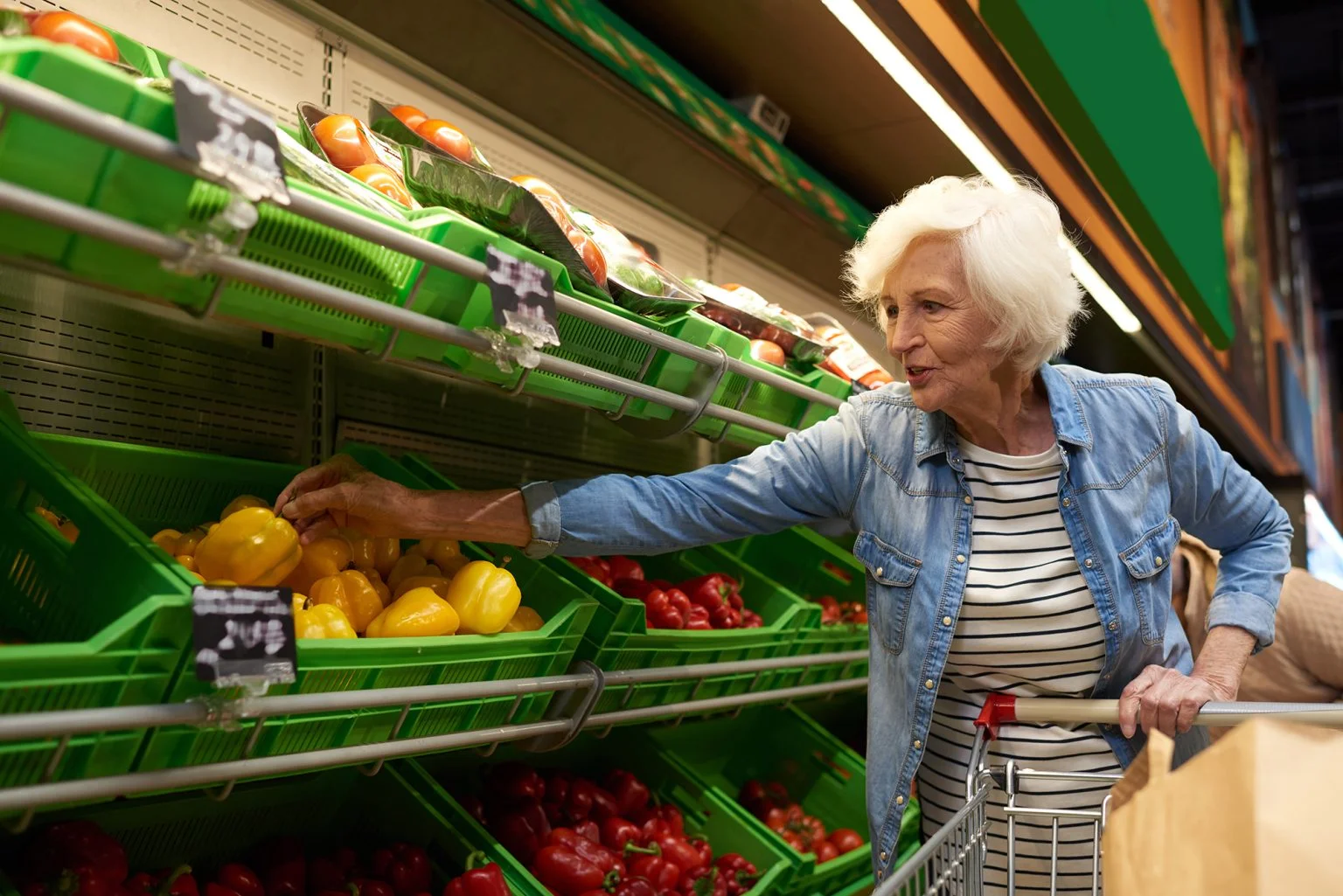 Portrait of modern senior woman with shopping cart choosing fruits and vegetables in supermarket