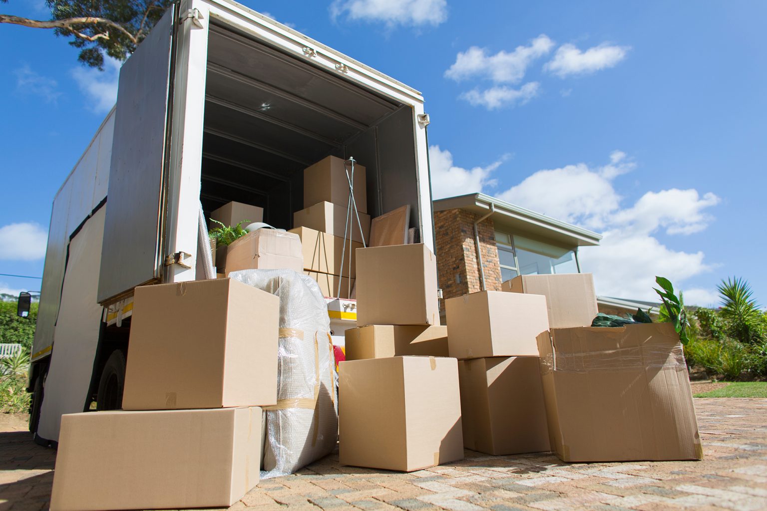 Cardboard boxes outside moving van and house in sunny driveway