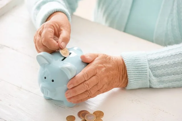 Senior woman putting coin into piggy bank at table