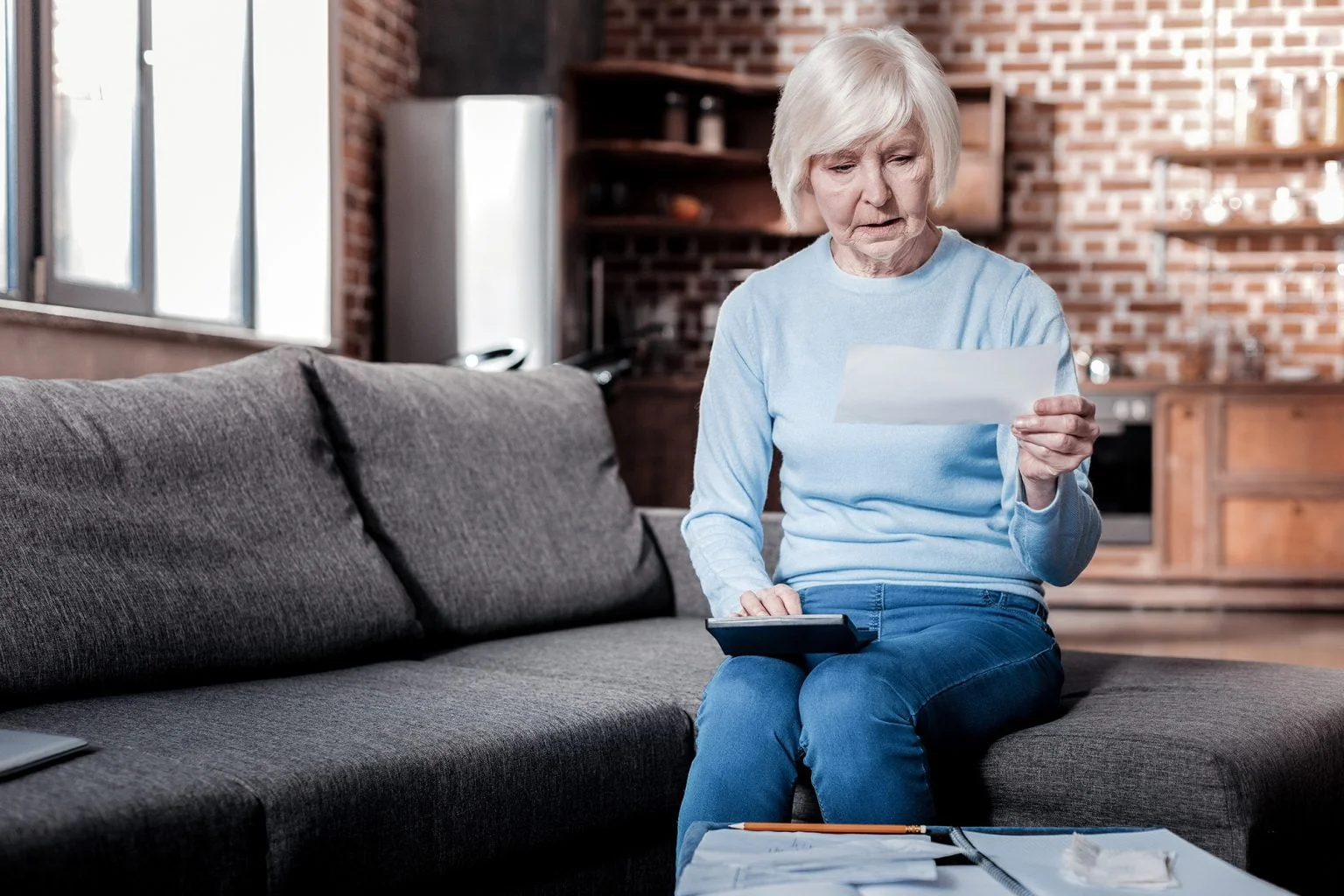 Serious pensioner bowing head while looking at check while sitting on a couch