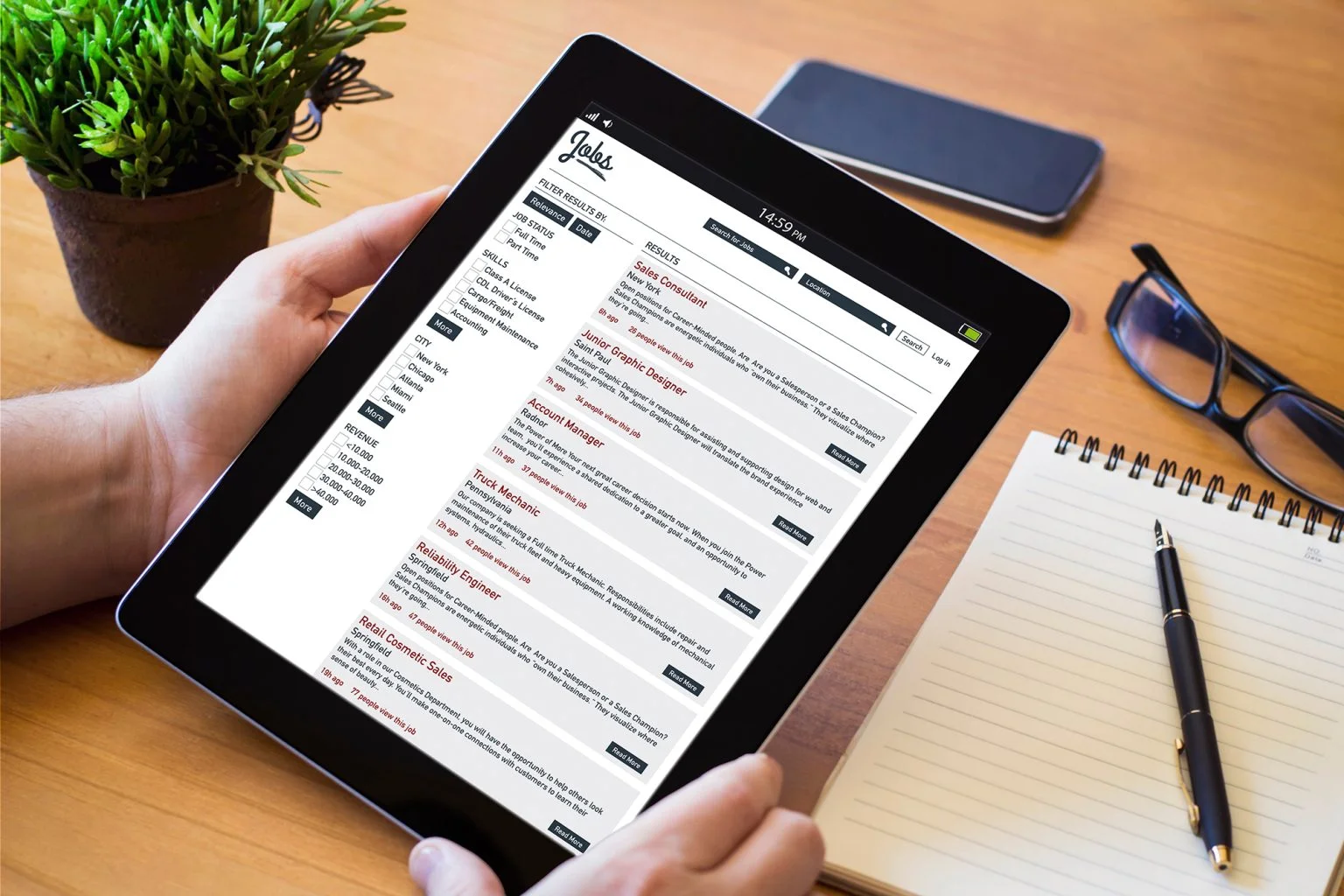 Job board website displayed on a tablet with a notepad, glasses, pen, and plant