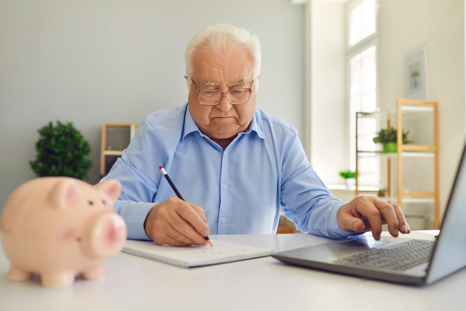 Retired man using laptop and taking notes in notebook studying pension plan and managing his budget