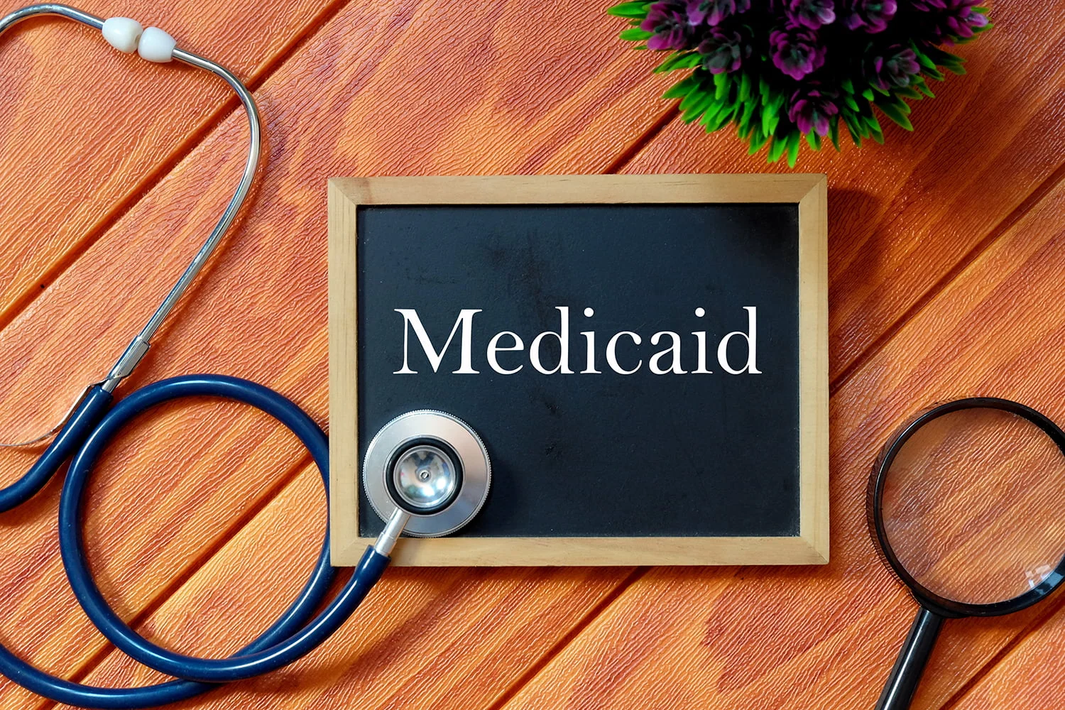 Top view of stethoscope,magnifying glass,plant and blackboard written with Medicaid on wooden background