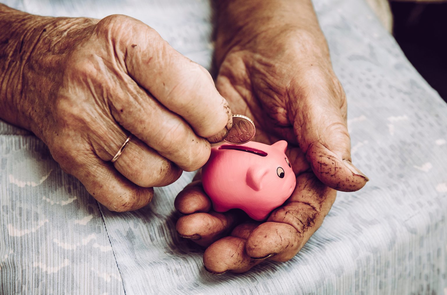 Close up of elderly woman's hands with tiny piggy bank