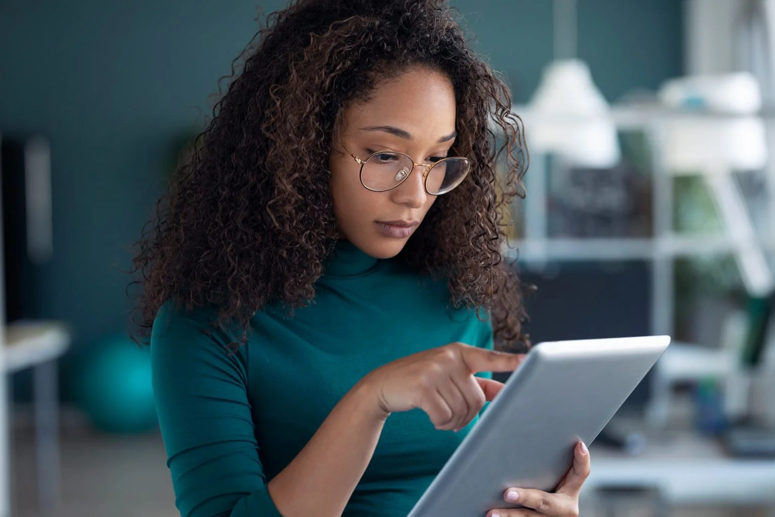 Concentrated young entrepreneur woman using her digital tablet while standing in the office