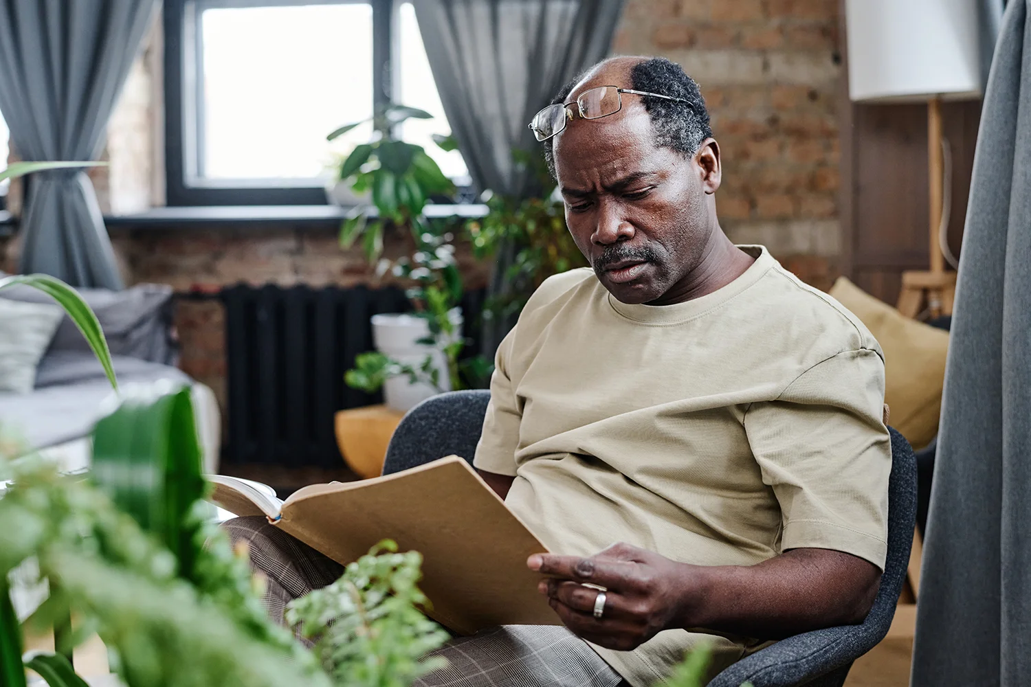 retired man sitting in armchair and reading curious book at leisure