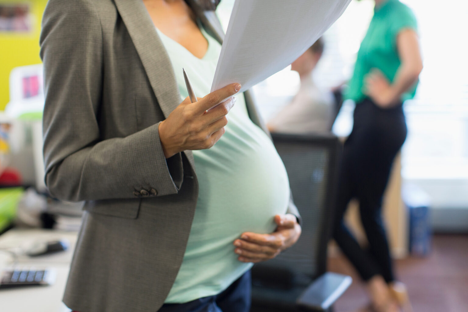 Pregnant businesswoman with paperwork holding stomach