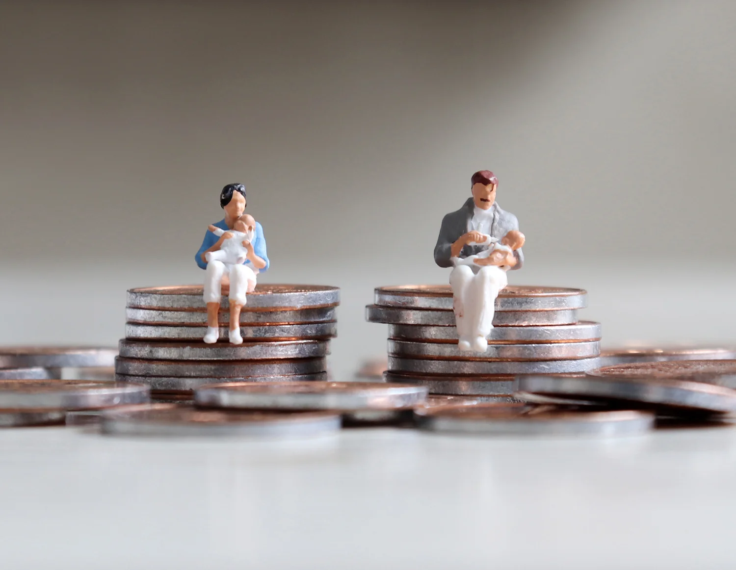 A miniature man and a miniature woman sitting with a baby on top of a stack of coins