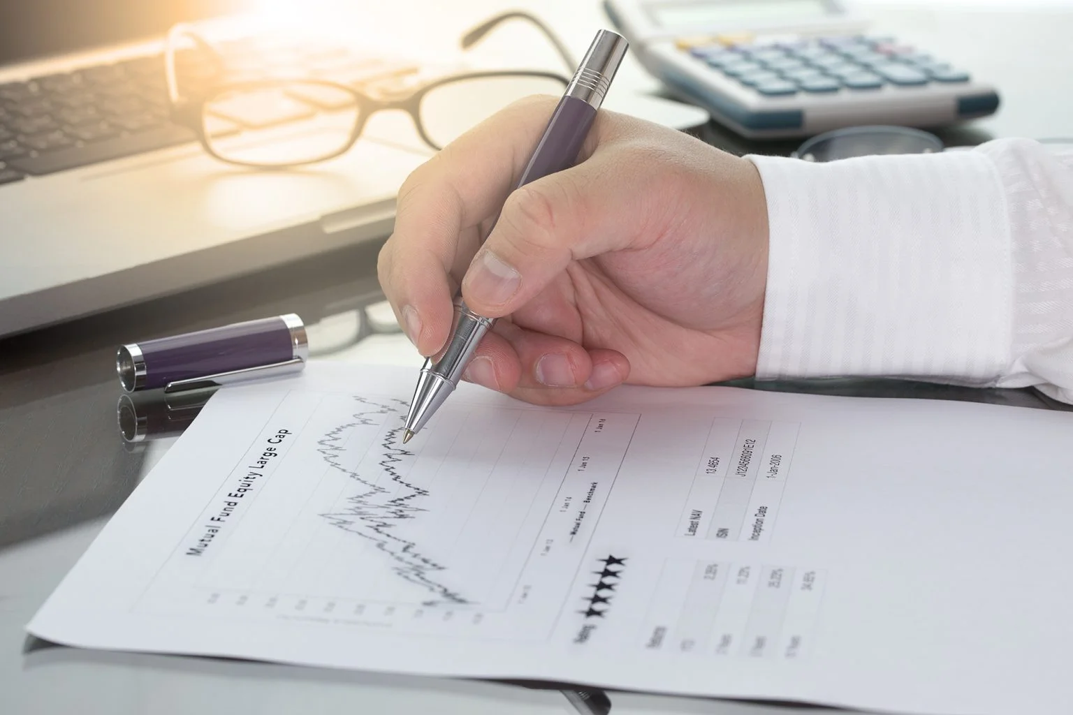 fund manager review Mutual Fund information with performance line graph and benchmark with pen calculator and computer laptop