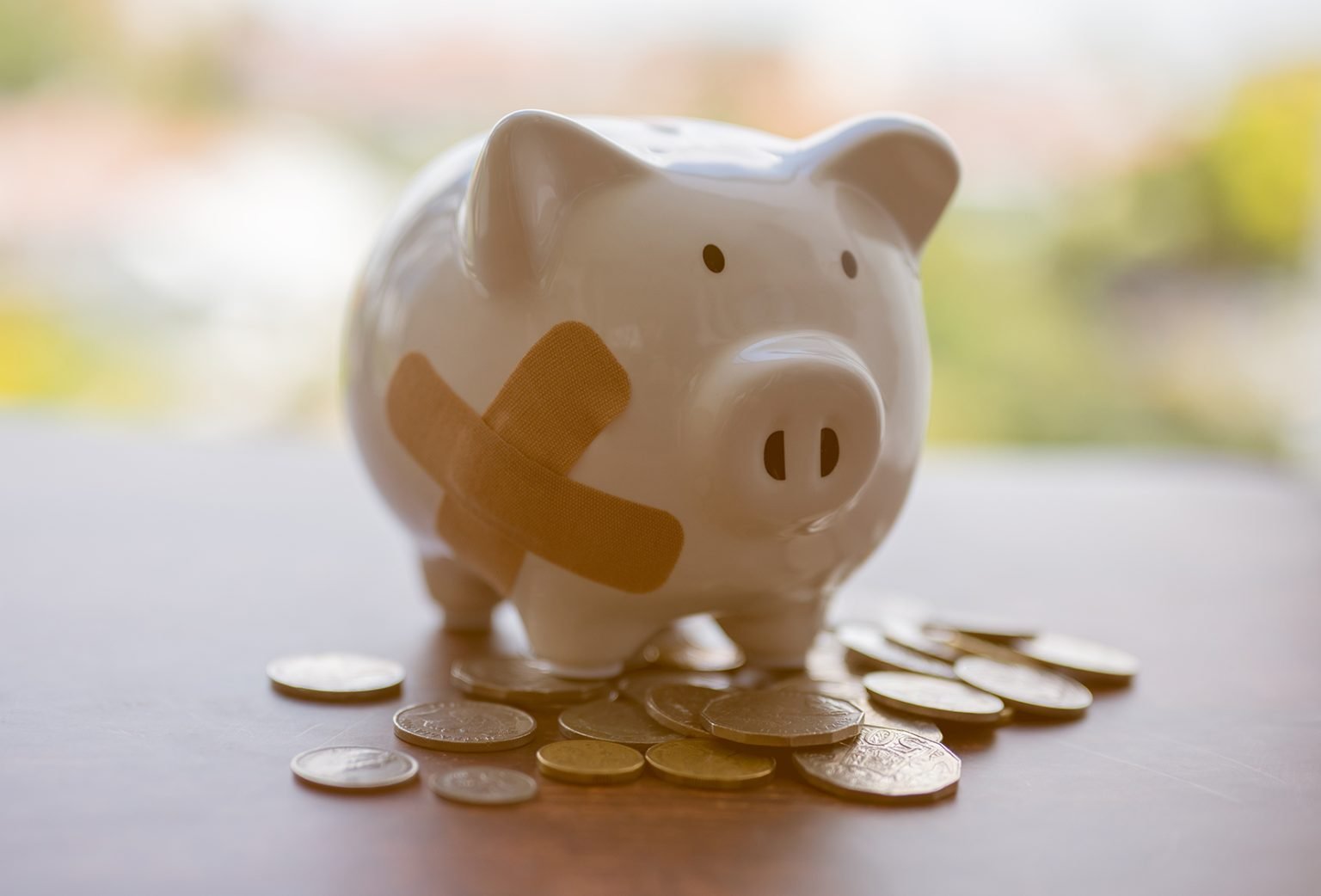 broken piggy bank with bandage standing on some coins