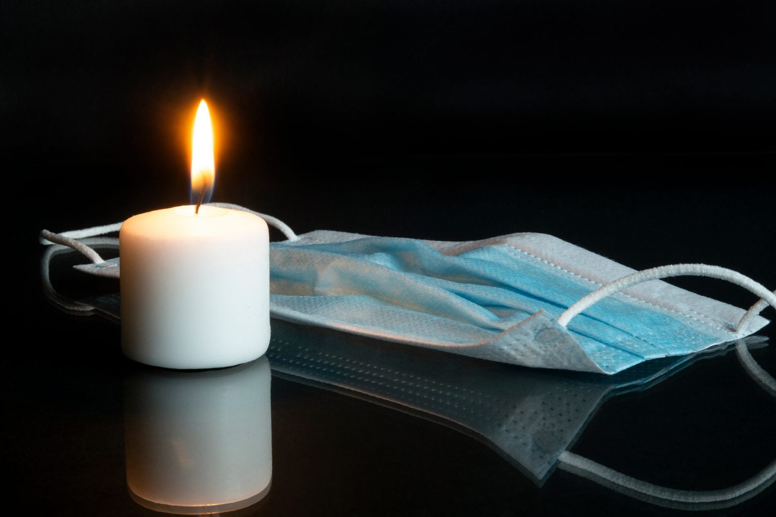 Lit candle and a COVID mask on a black background