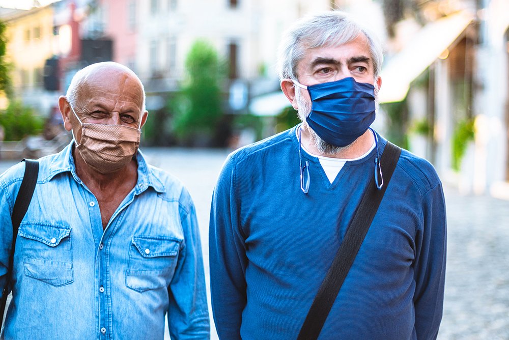 Two elderly citizens walking in the street with COVID masks