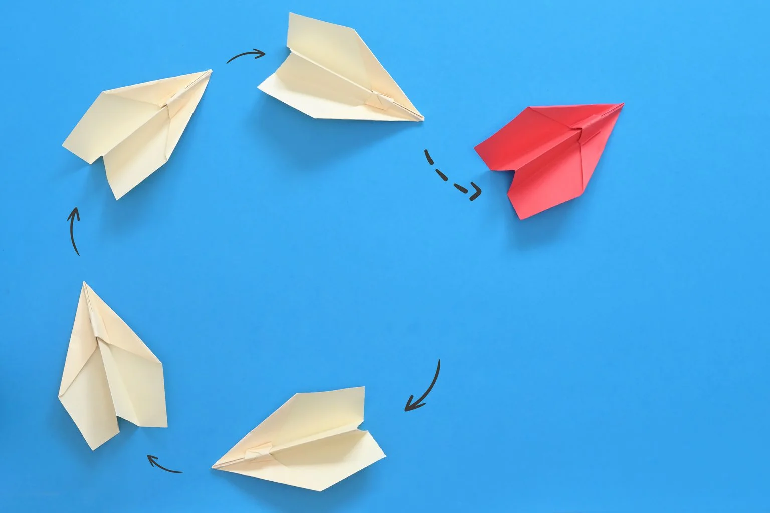 white paper airplanes in a circle with one red paper airplane changing direction