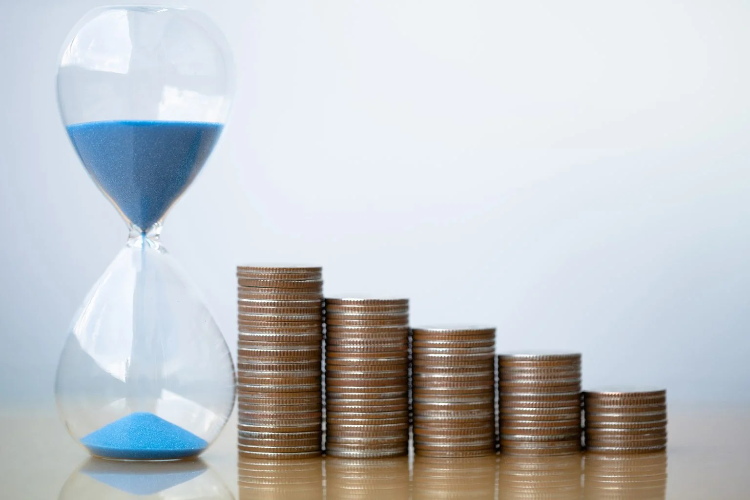 Hourglass blue sand and stack of coins