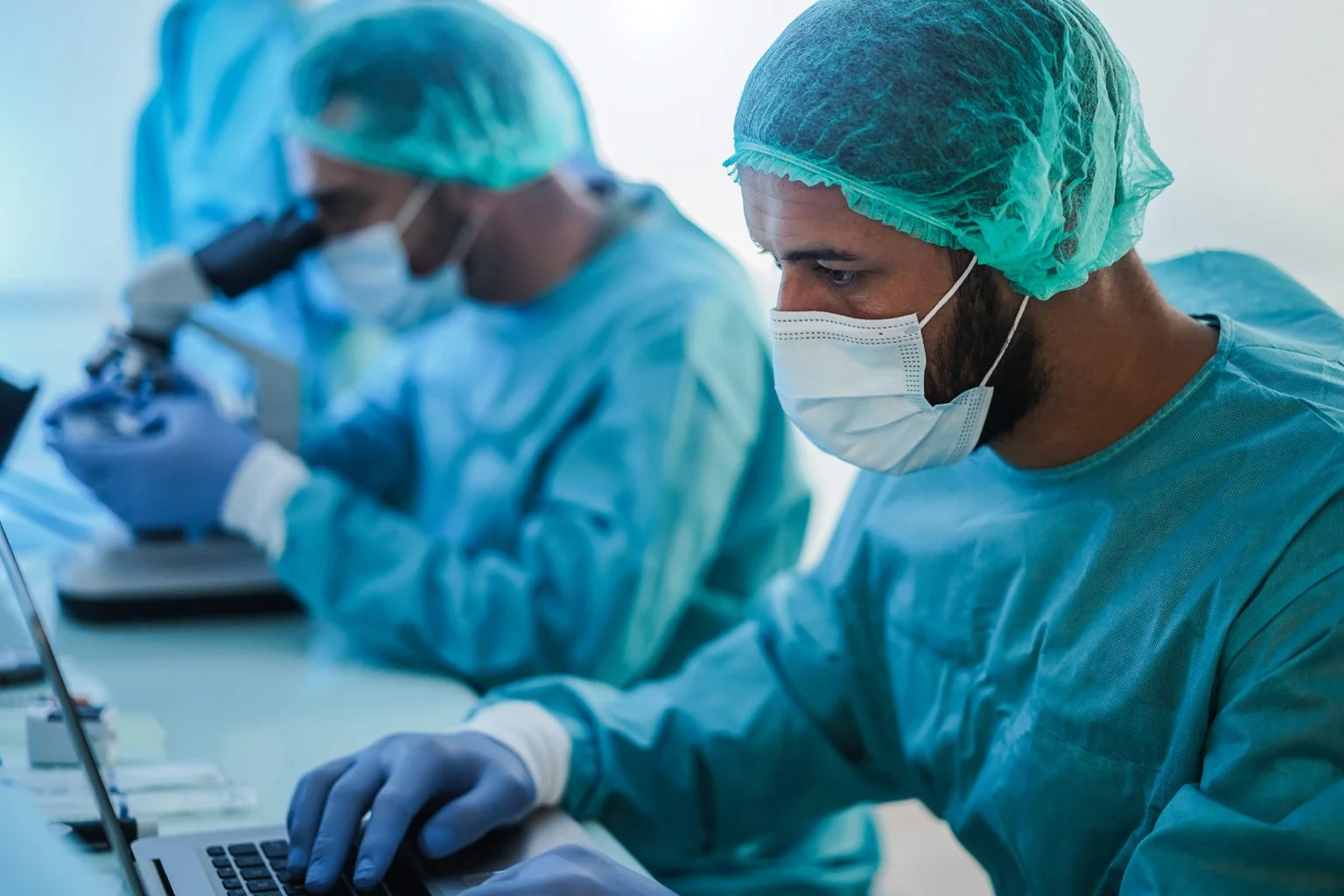Medical workers in hazmat suit working with laptop computer and micoroscope inside laboratory hospital during coronavirus outbreak