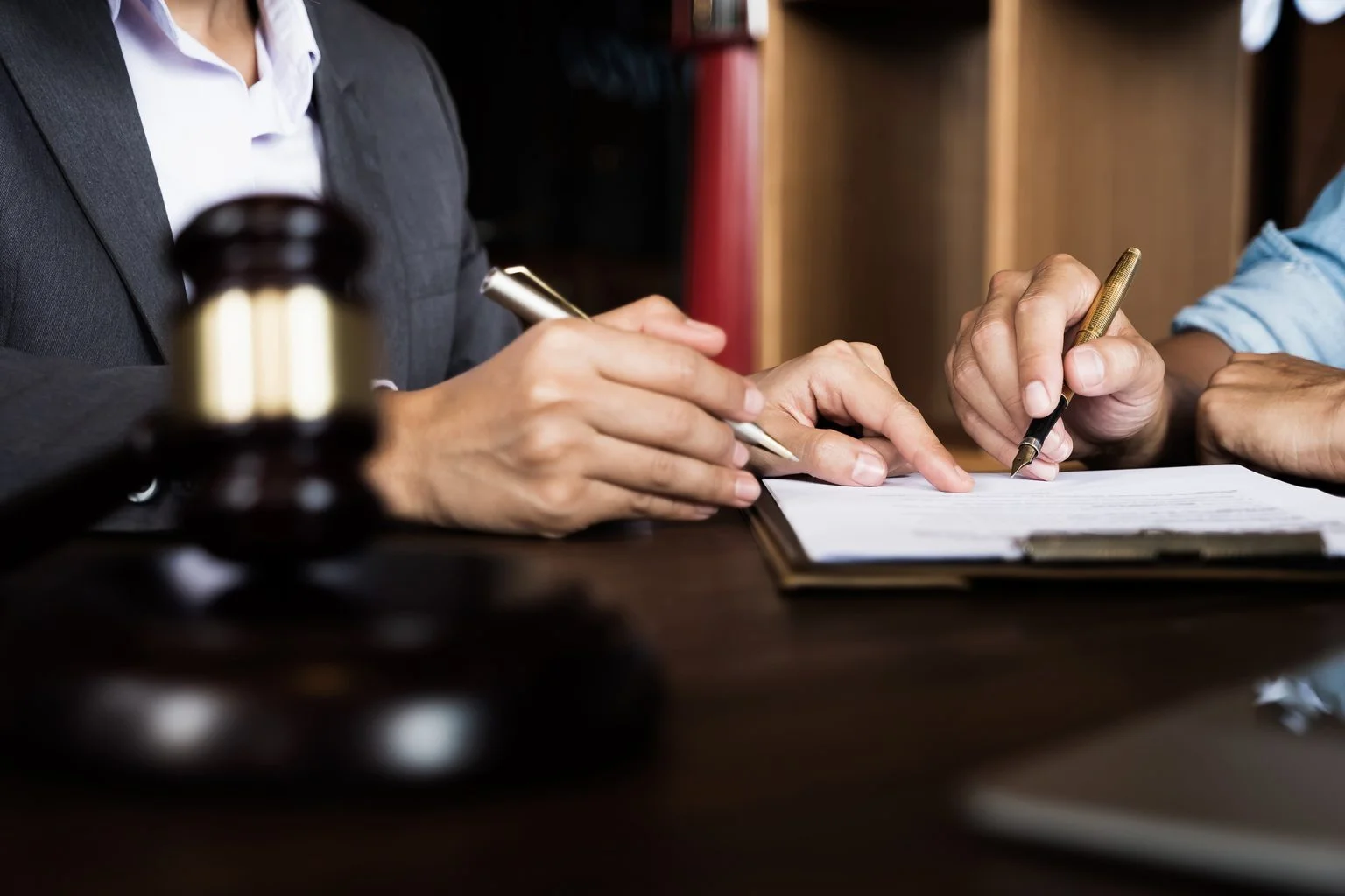 Two people signing documents behind a gavel