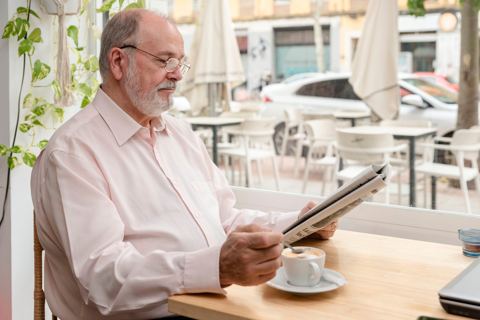 older man in glasses reading a daily newspaper while drinking his coffee