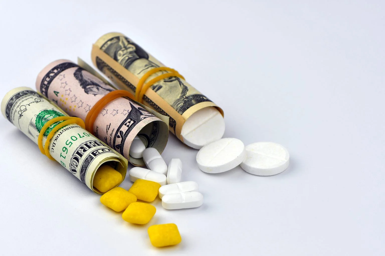 Dollar rolled up with pills flowing out isolated on white background