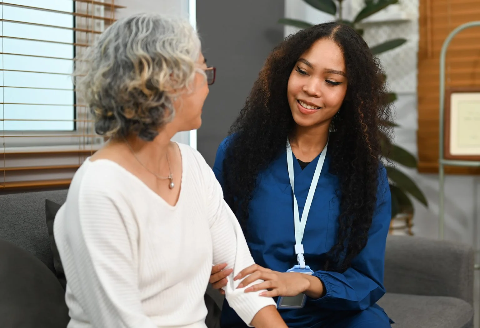 Elderly woman talking with caring young nurse, receiving home care