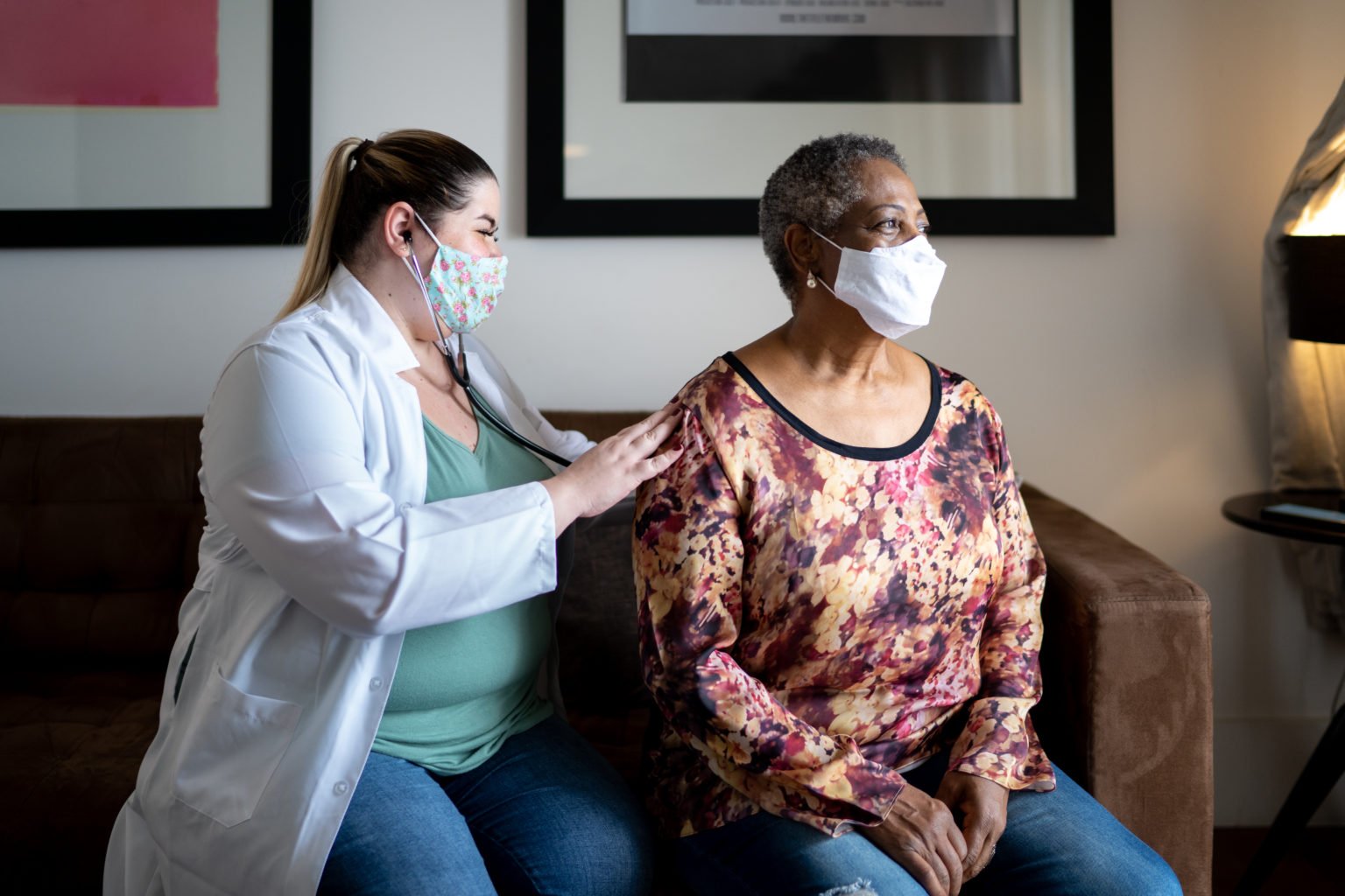 Doctor using stethoscope listening to senior patient breathing at her house – using face mask