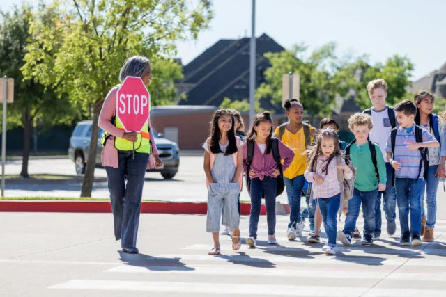 Female crossing guard leads children safely across street