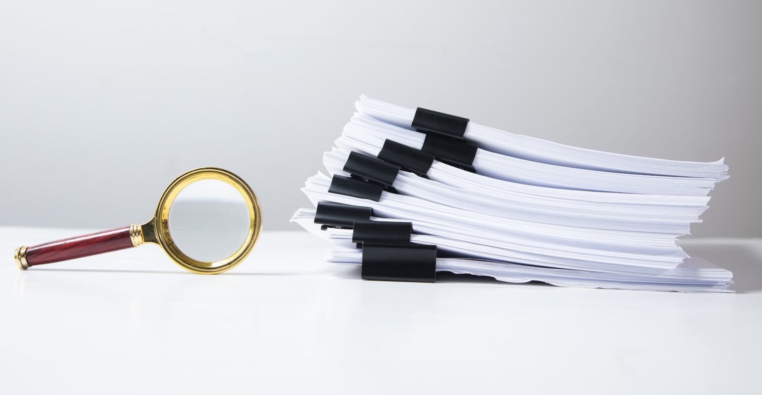Stack of report paper documents with magnifying glass.