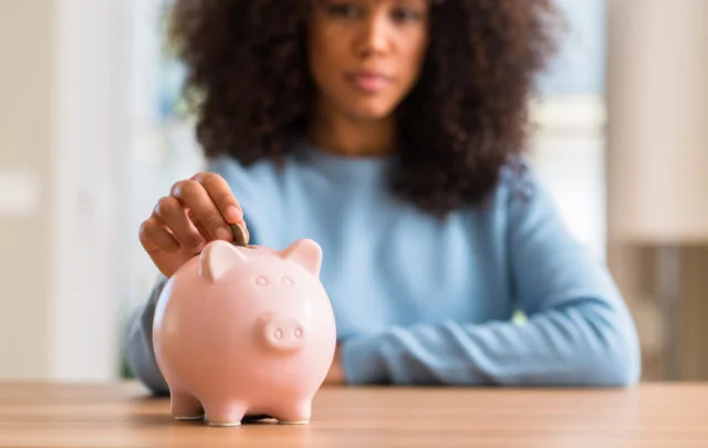 African american woman saves money in piggy bank with a confident expression on smart face thinking serious