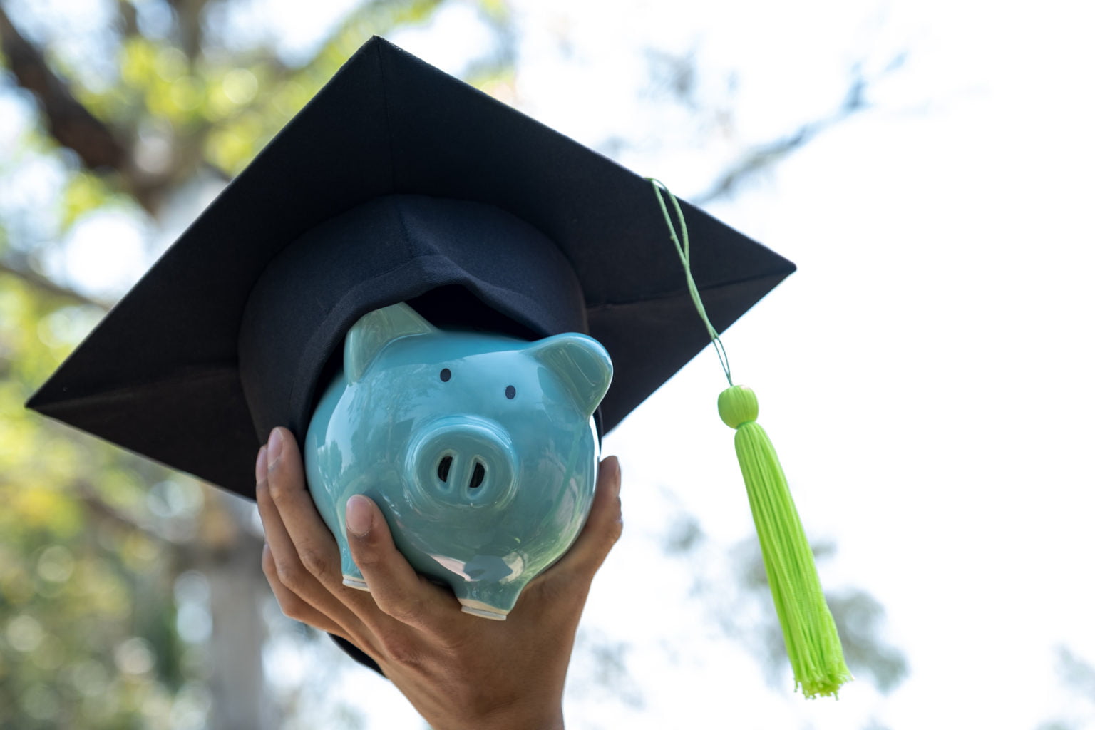Hand holding Blue piggy bank with  graduation hat, Saving money