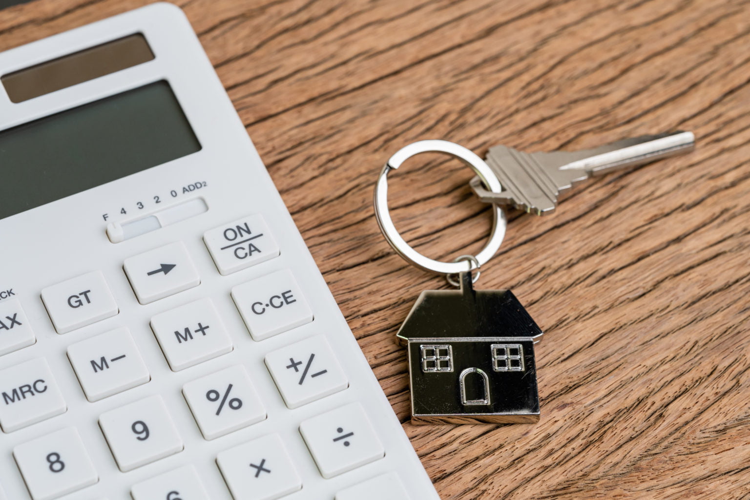 Home key with house keychain with white calculator on wooden table