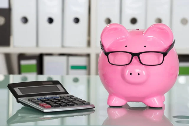 Piggybank Wearing Eyeglasses and Calculator on Desk