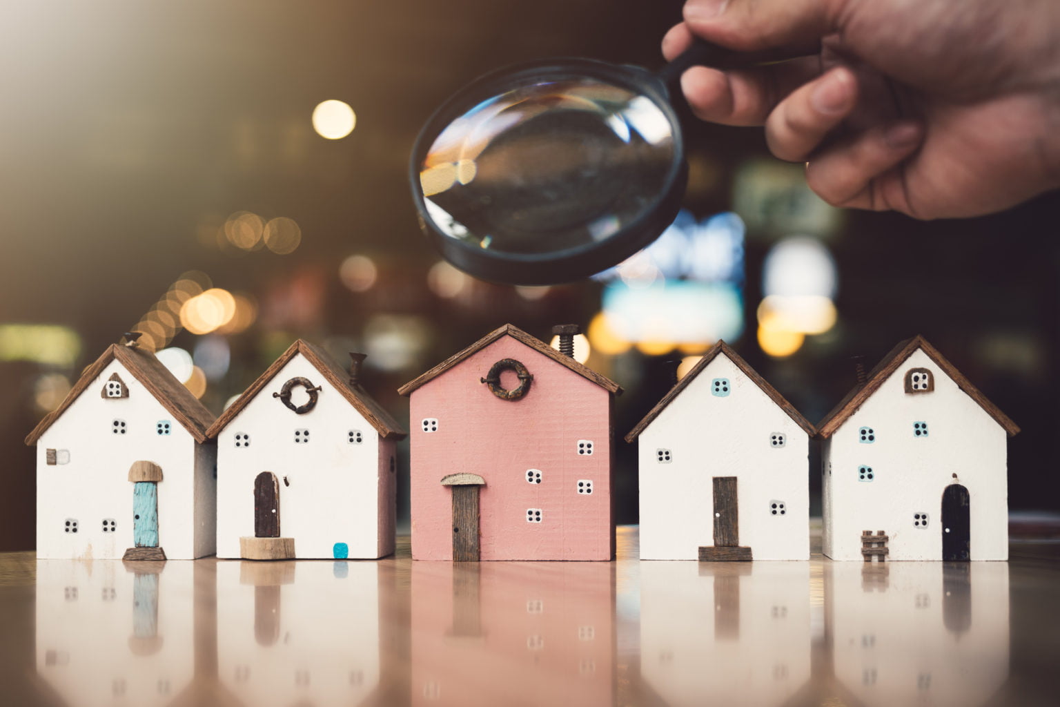 Hand holding magnifying glass and looking at house model, house