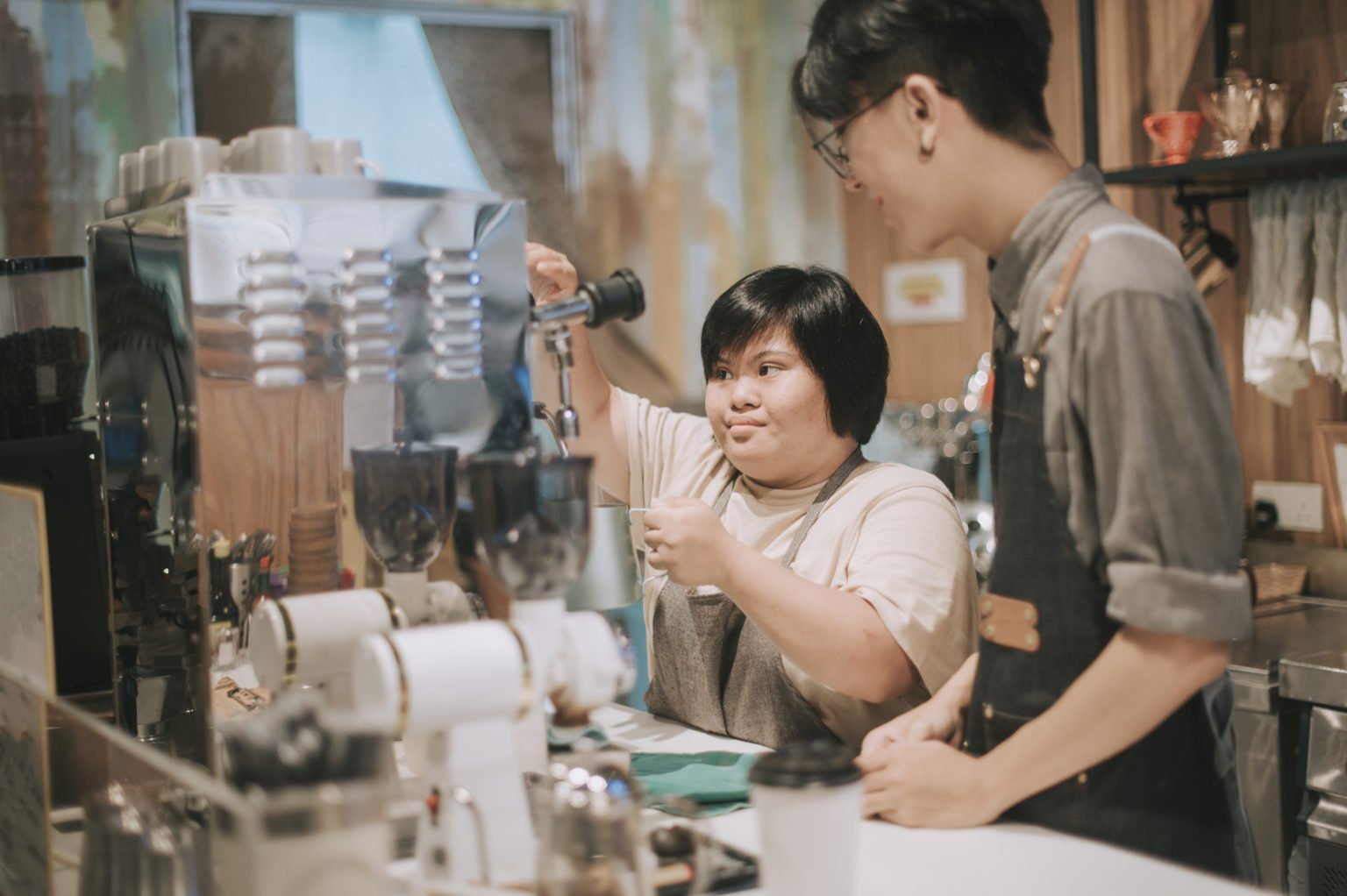 asian down syndrome female learning from barista making coffee in her café place of work