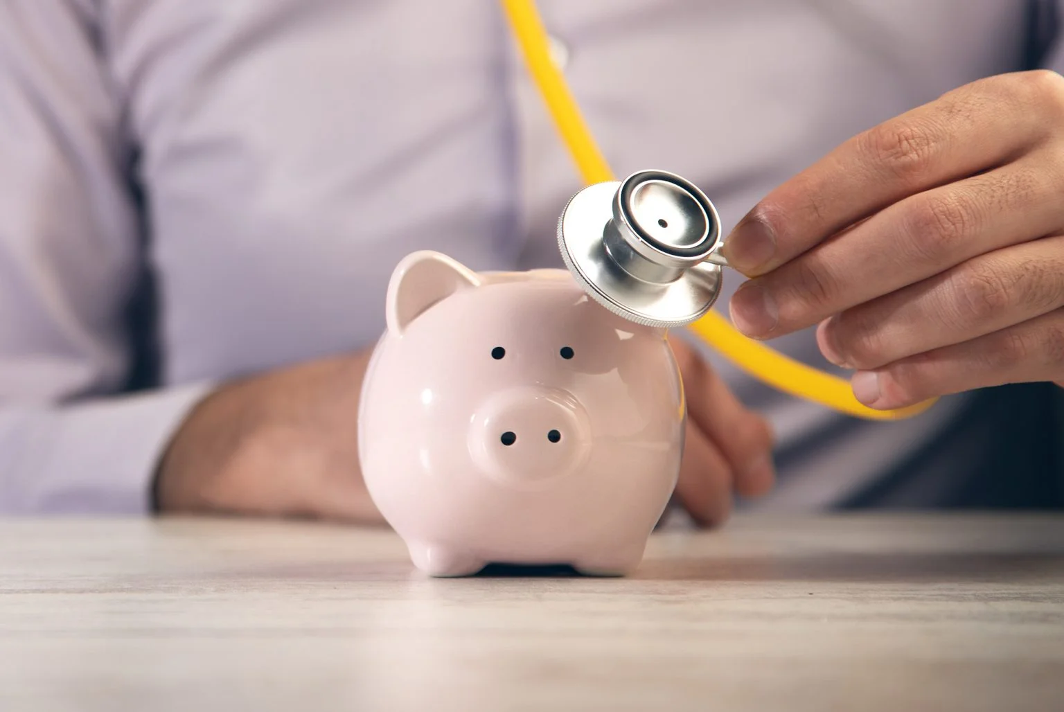 man holding stethoscope with piggy bank