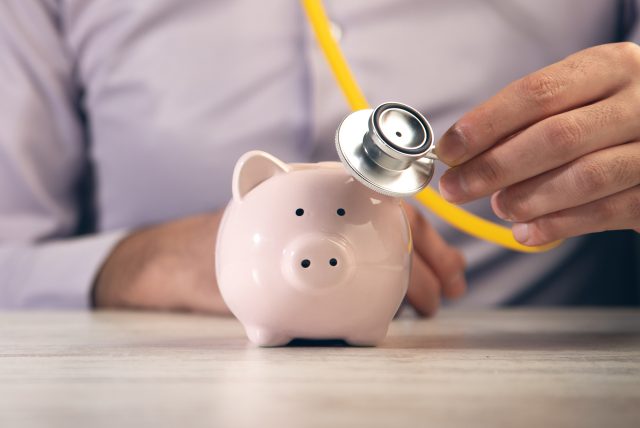 man holding stethoscope with piggy bank