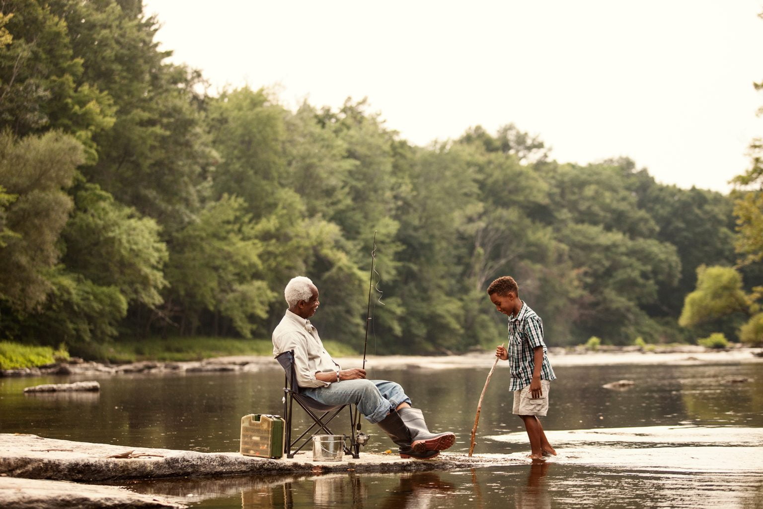 Boy (6-7) fishing with senior man by river