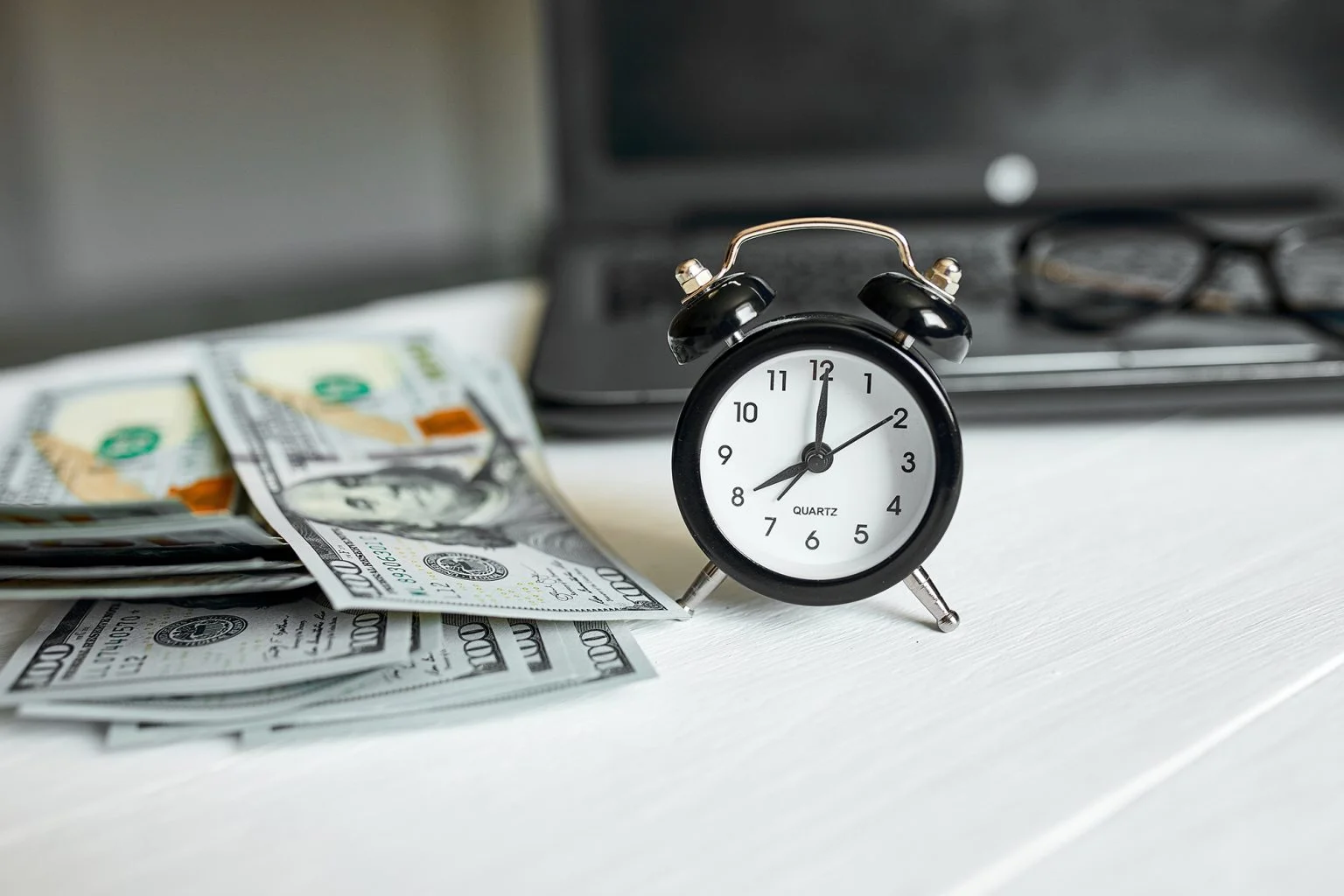 Modern workplace of laptop, clock, money, dollars banknote with copy space on white wooden background