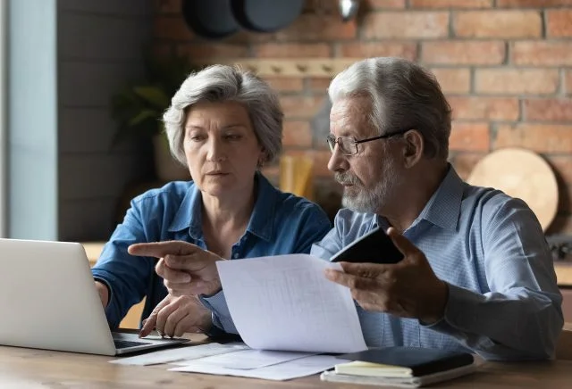 Older couple sitting at a table looking at laptop screen paying bills online