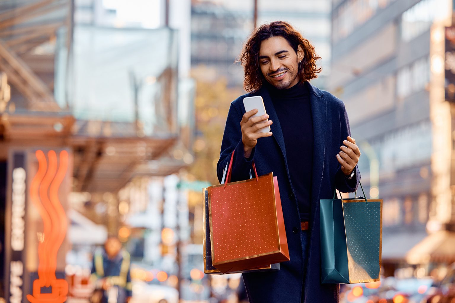 Young man looking at a cell phone with shopping bags on a city street
