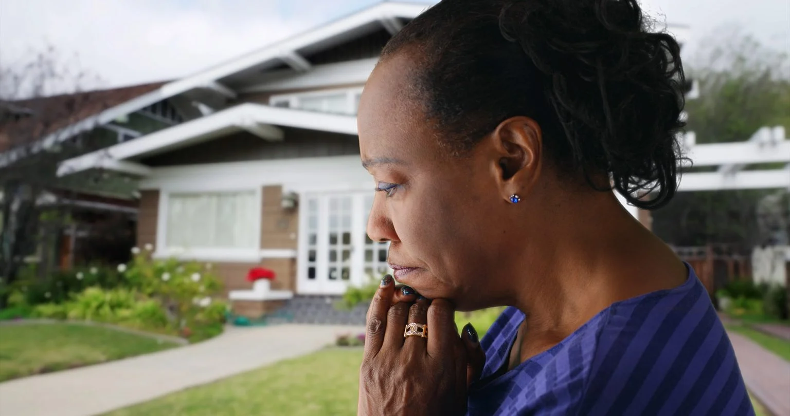 An older woman looking concerned in front of her house