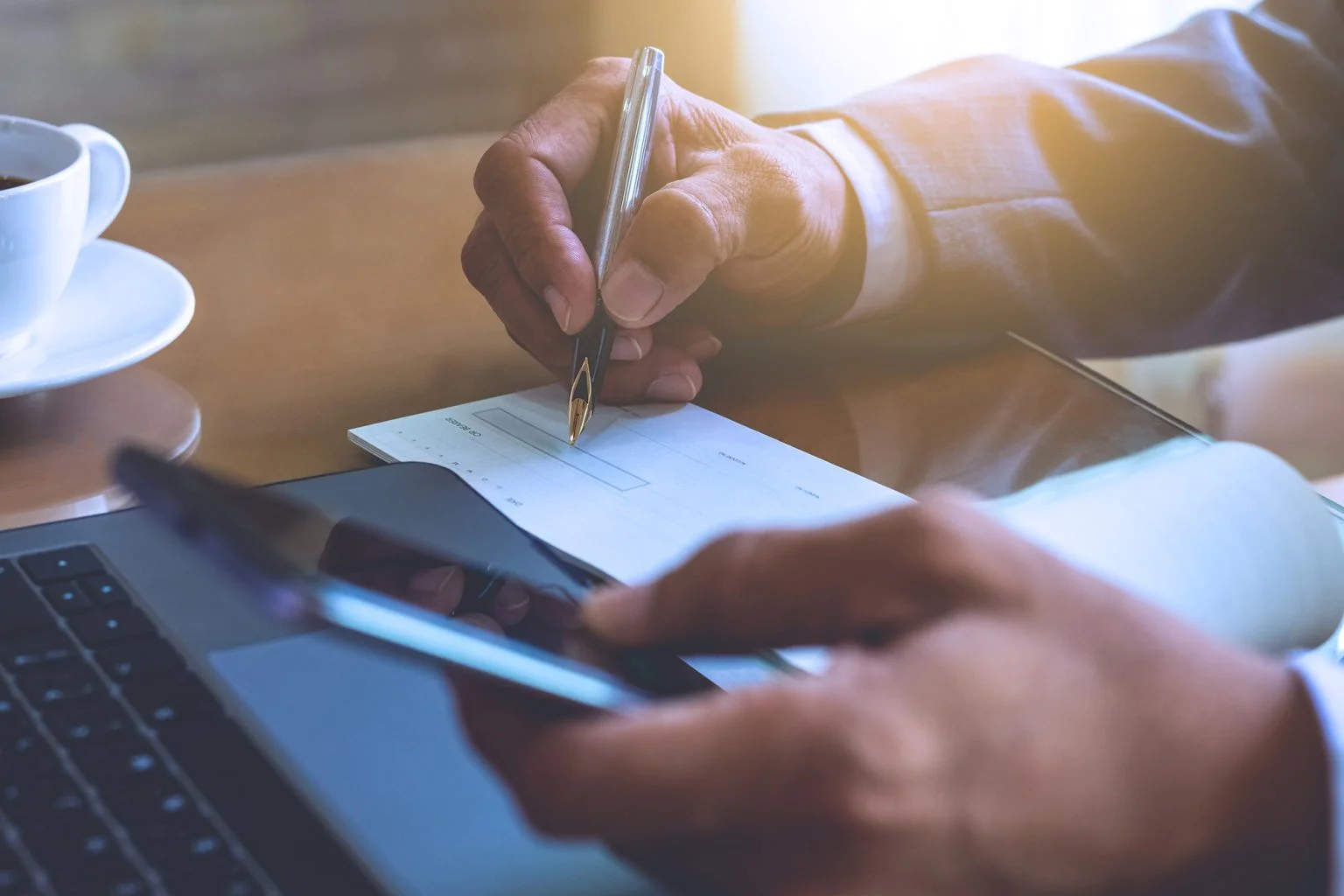 Man hand holding mobile smart phone and signing checkbook on the desk at office