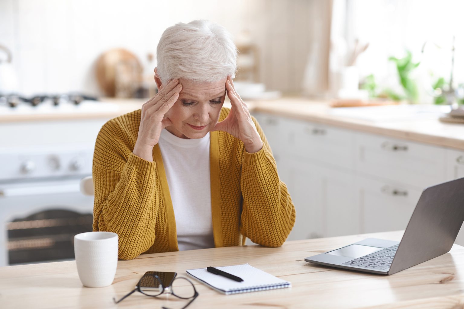 Stressed older woman looking at notepad at a kitchen counter