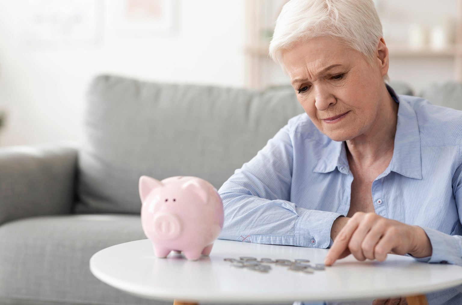 Upset elderly woman counting coins from piggy bank