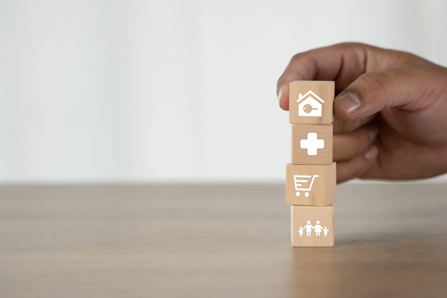 Wooden blocks showing a family, a shopping cart, a medical cross, and a house