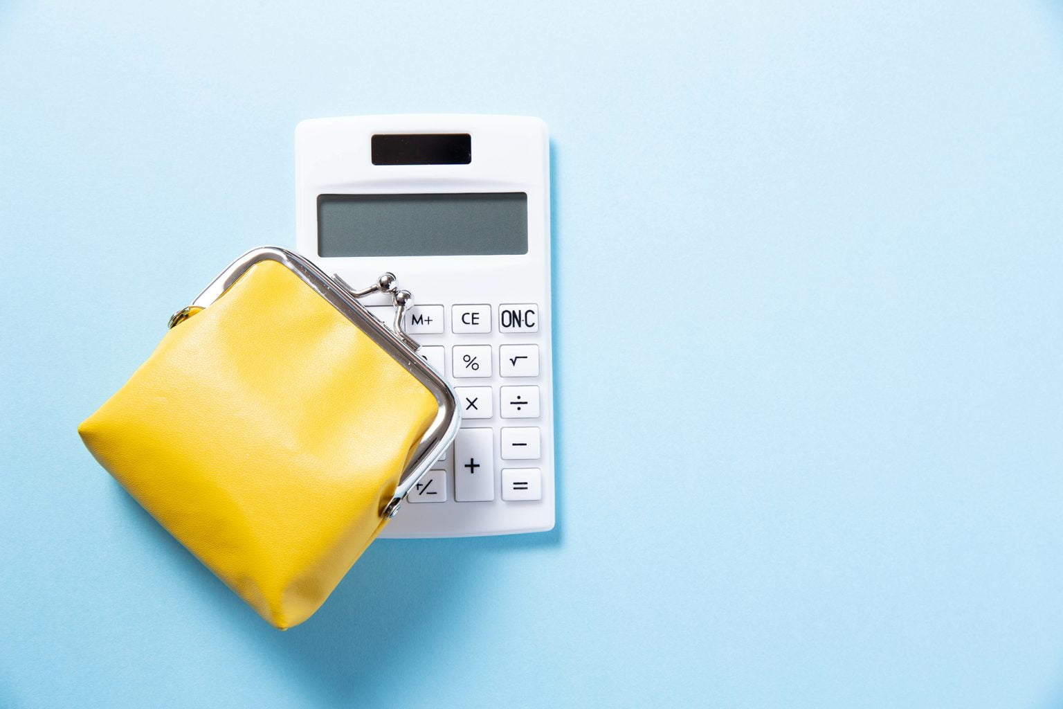 Yellow coin purse on top of a white calculator on a blue background