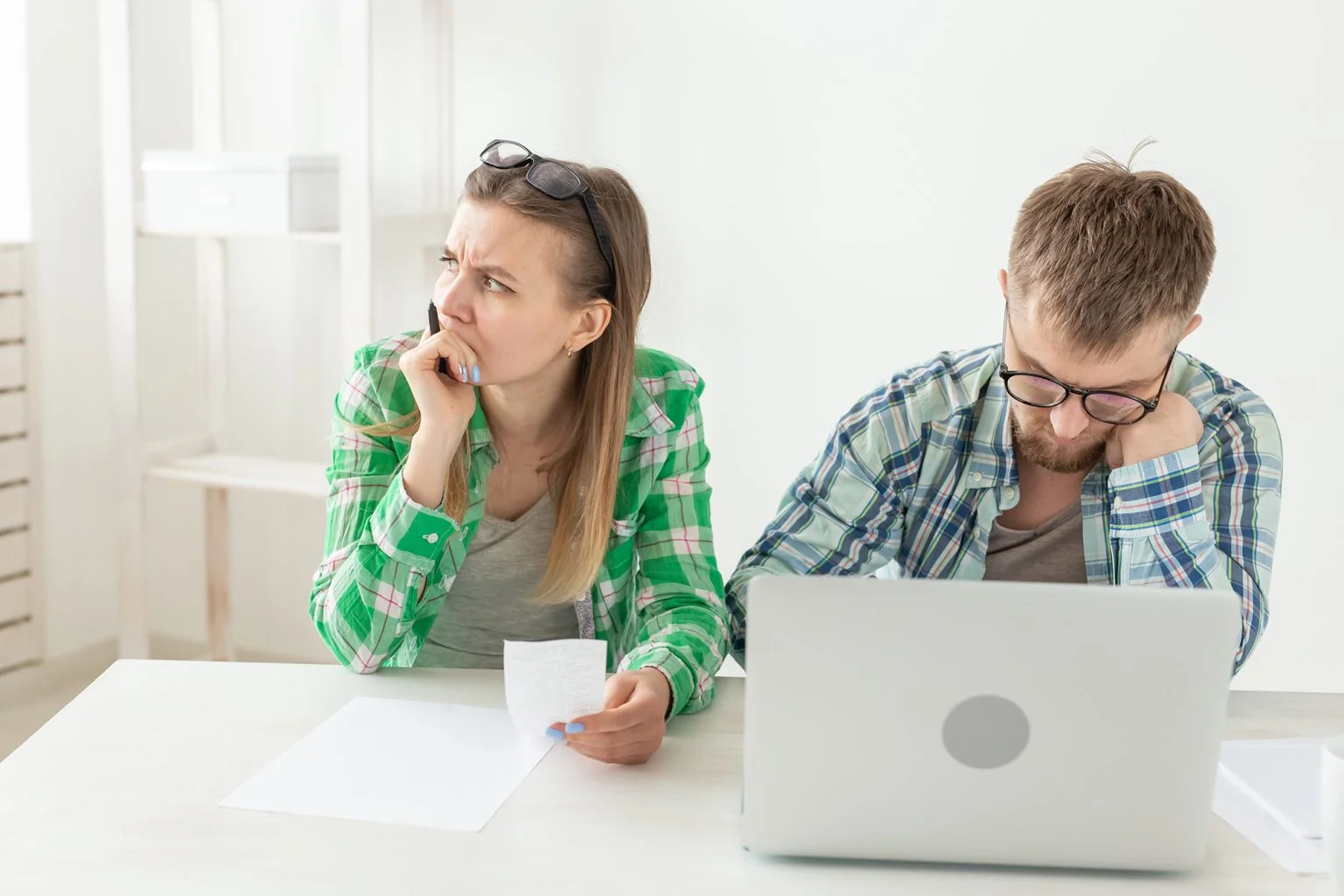 Young husband and wife are upset about numerous checks for payments and purchases for repairs while sitting at the table with a laptop