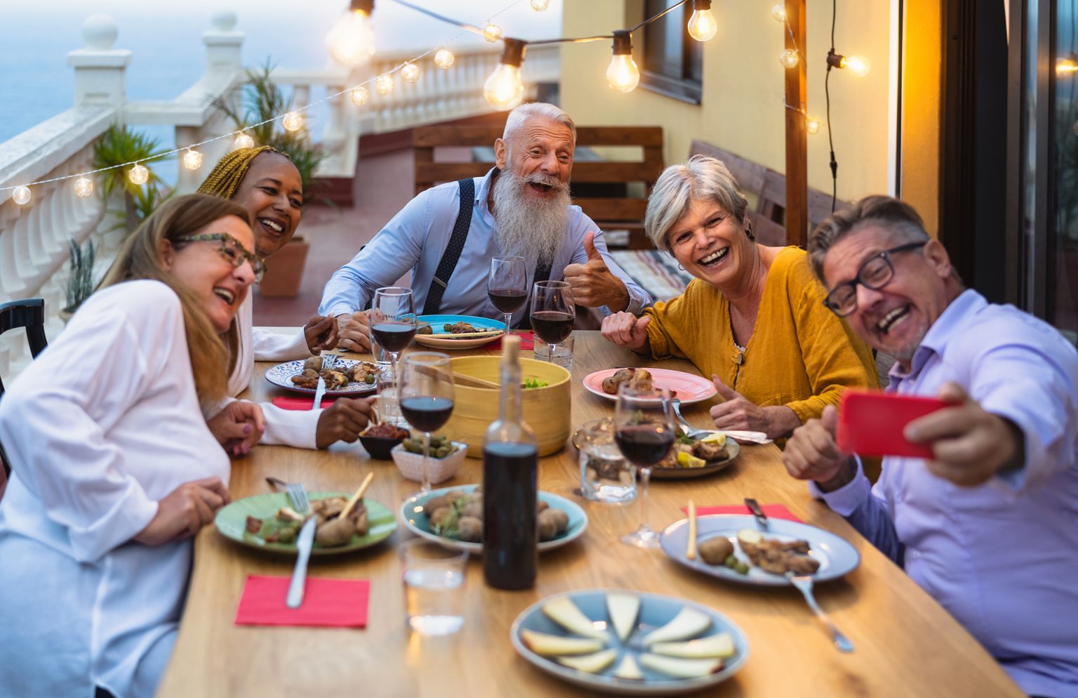 senior friends having fun dining together while taking selfie with mobile smartphone on house patio